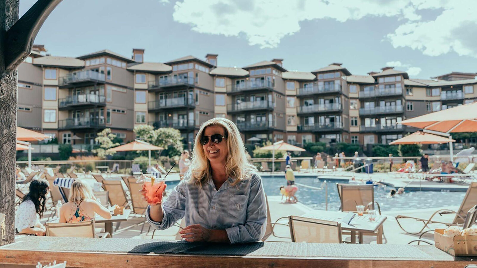 A woman enjoying a drink after a day on the golf course at outdoor seating by the swimming pool at The Cove resort, home to The Landing Kitchen, one of Kelowna's best seafood restaurants, steak houses, and full bar with casual dining options