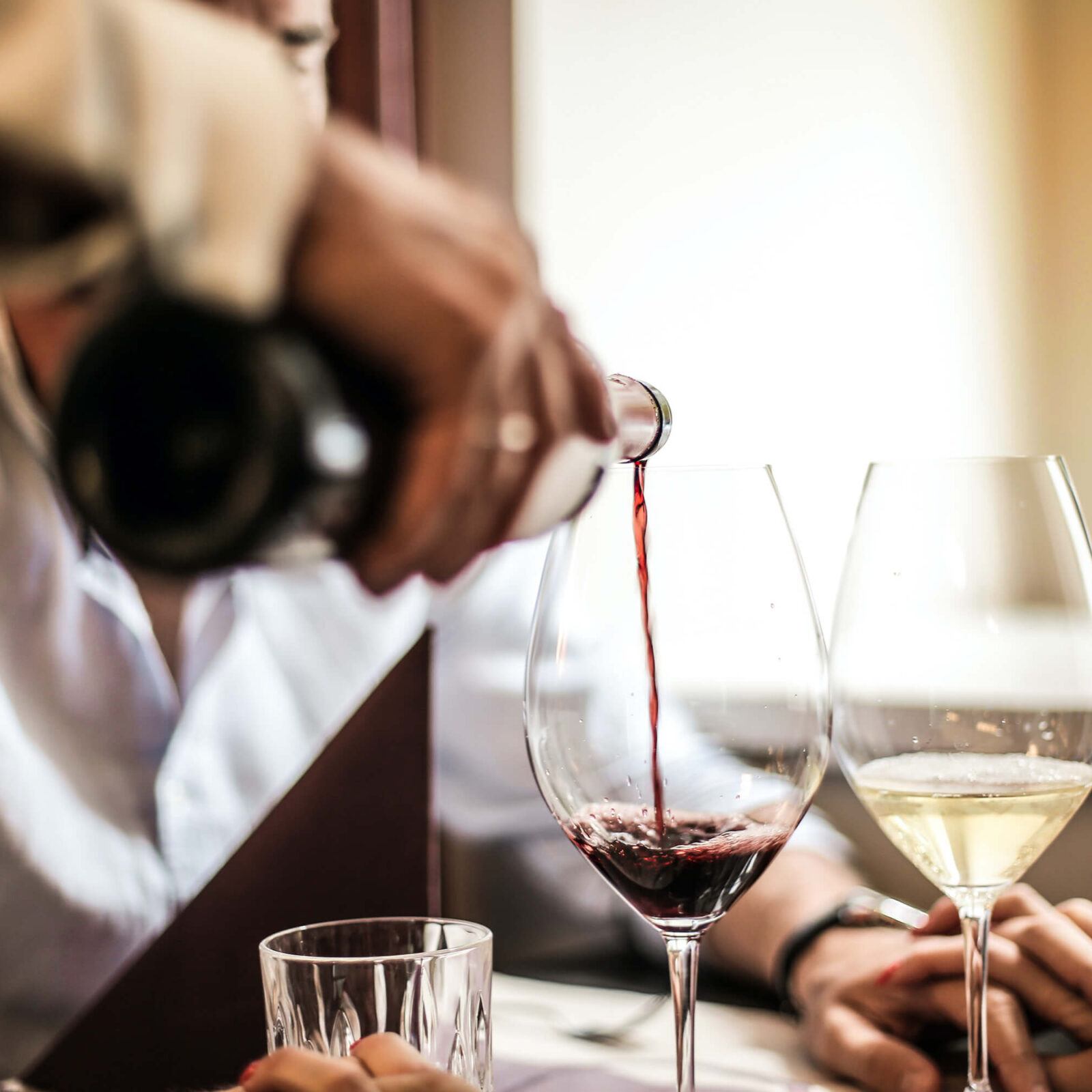 A server pouring red wine from Mission Hill Winery into a glass during happy hour before the main course of fresh seafood arrives at The Landing West Kelowna restaurants
