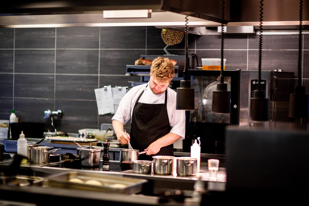 An experienced chef at the Landing Kitchen in West Kelowna, BC - dine in and takeout restaurants - preparing a sauce for a seafood platter in a modern restaurant kitchen known for great food, great service, and generous portion sizes