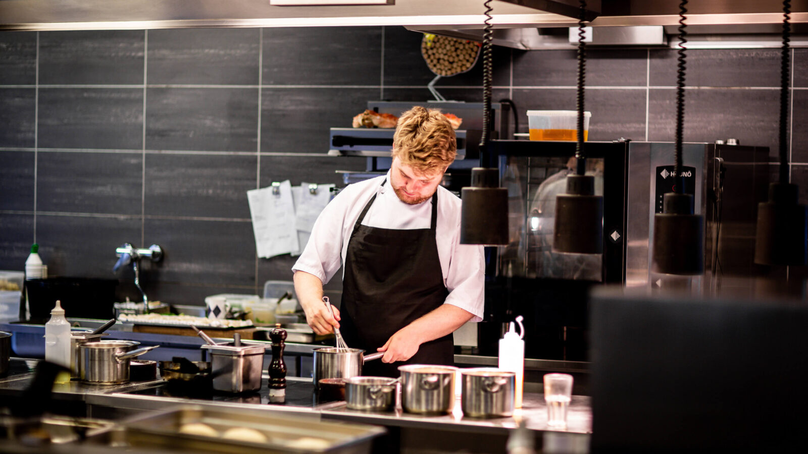 An experienced chef preparing a sauce for a seafood platter in a modern restaurant kitchen known for tasty dishes